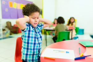 Overwhelmed preschooler with autism in kindergarten Upset autistic little boy covering his ears and feeling distressed and overwhelmed by the loud noises in preschool